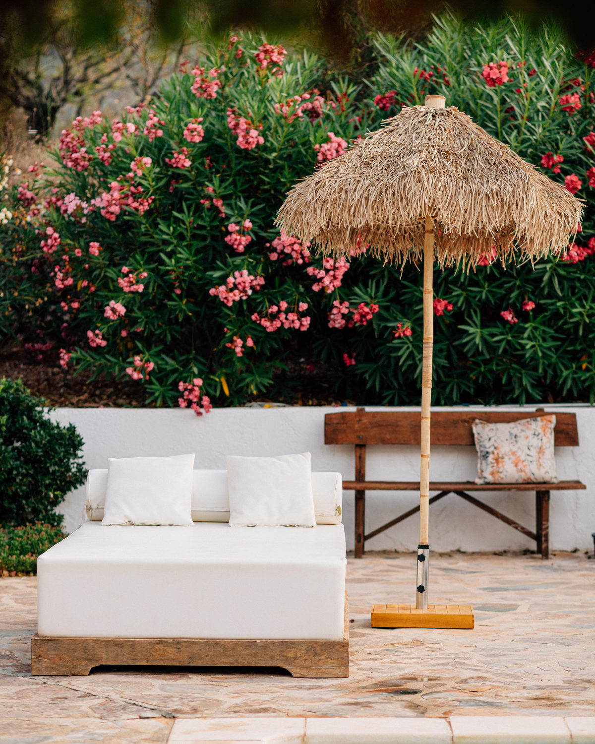 Daybed beneath oleander flowers and a thatched parasol